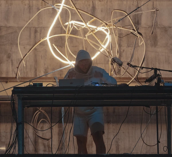 Musiker Fredrik Høyer står bak en miksepult og spiller musikk med en futuristisk lampe i bakgrunnen. Foto.